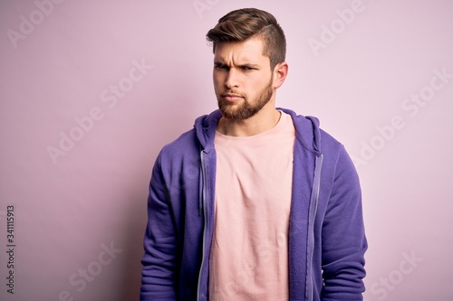 Young blond man with beard and blue eyes wearing purple sweatshirt over pink background skeptic and nervous, frowning upset because of problem. Negative person. © Krakenimages.com