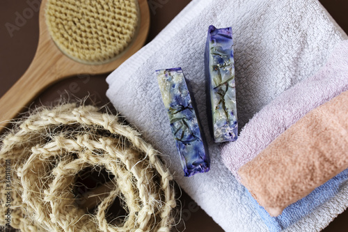 White towel, washcloth, dry massage brush and hand made lavender soapы on the brown background. Home spa in isolation.
