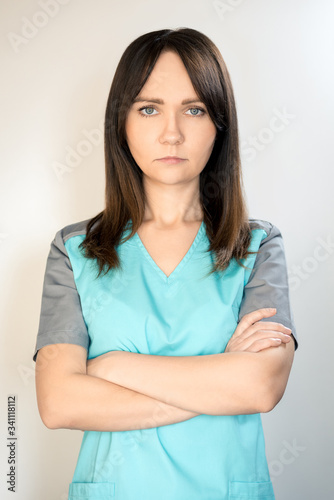 The topic of coronavirus and safety. Young serious female doctor in a surgical suit on a light background. Vertical frame © Алексей Еремеев