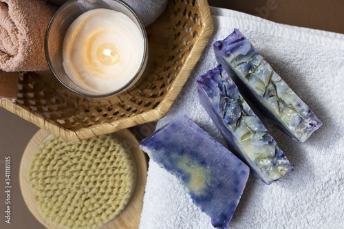 White, blue, coral, purple towels, washcloth, dry massage brush and hand made lavender soaps, candle on the brown background. Home spa in isolation. Zero waste concept.