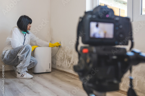 Video camera filming how woman using dehumidifier cleaning and drying air next to a bad mold and fungus growth on an interior wall. photo