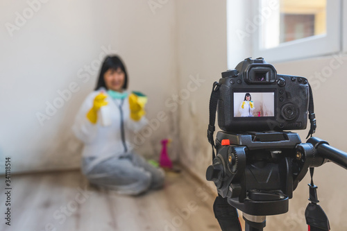 Video camera filming woman cleaning mold from wall using spray bottle and sponge.