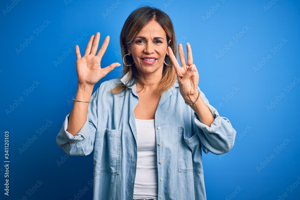 Middle age beautiful woman wearing casual shirt standing over isolated blue background showing and pointing up with fingers number eight while smiling confident and happy. Middle age beautiful woman wearing casual shirt standing over isolated blue background showing and pointing up with fingers number eight while smiling confident and happy.