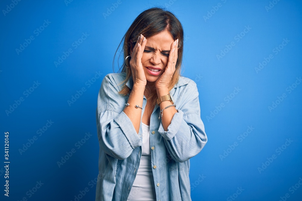 Middle age beautiful woman wearing casual shirt standing over isolated blue background with hand on headache because stress. Suffering migraine. Middle age beautiful woman wearing casual shirt standing over isolated blue background with hand on headache because stress. Suffering migraine.