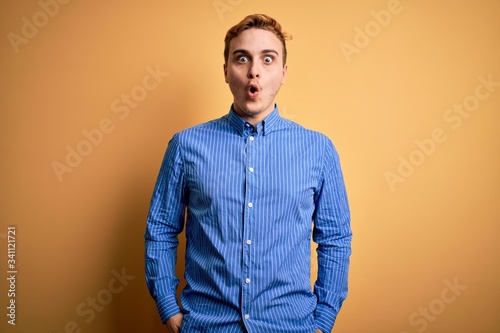 Young handsome redhead man wearing casual striped shirt over isolated yellow background afraid and shocked with surprise expression, fear and excited face.