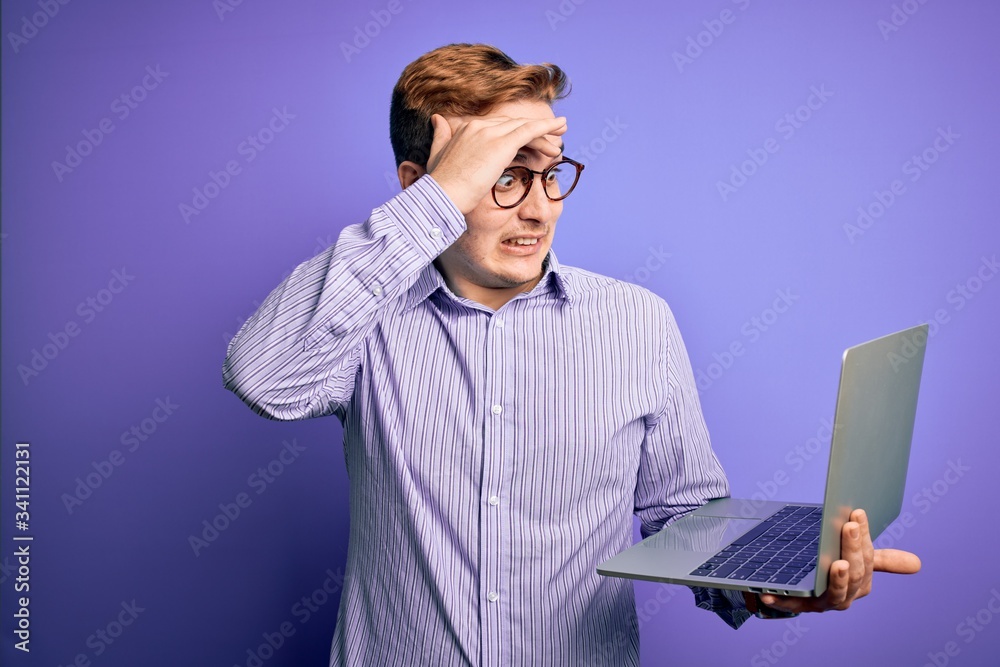 Young handsome redhead businessman working using laptop over purple background stressed with hand on head, shocked with shame and surprise face, angry and frustrated. Fear and upset for mistake. Young handsome redhead businessman working using laptop over purple background stressed with hand on head, shocked with shame and surprise face, angry and frustrated. Fear and upset for mistake.