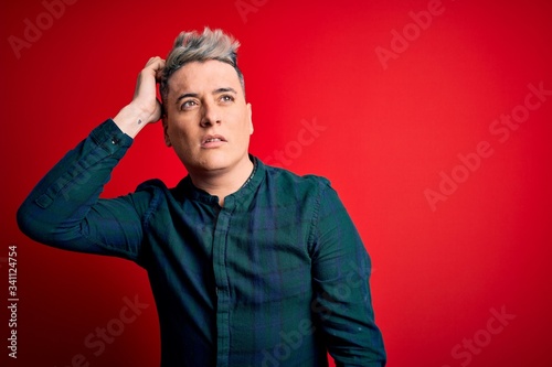 Young handsome modern man wearing elegant green shirt over red isolated background confuse and wondering about question. Uncertain with doubt, thinking with hand on head. Pensive concept.