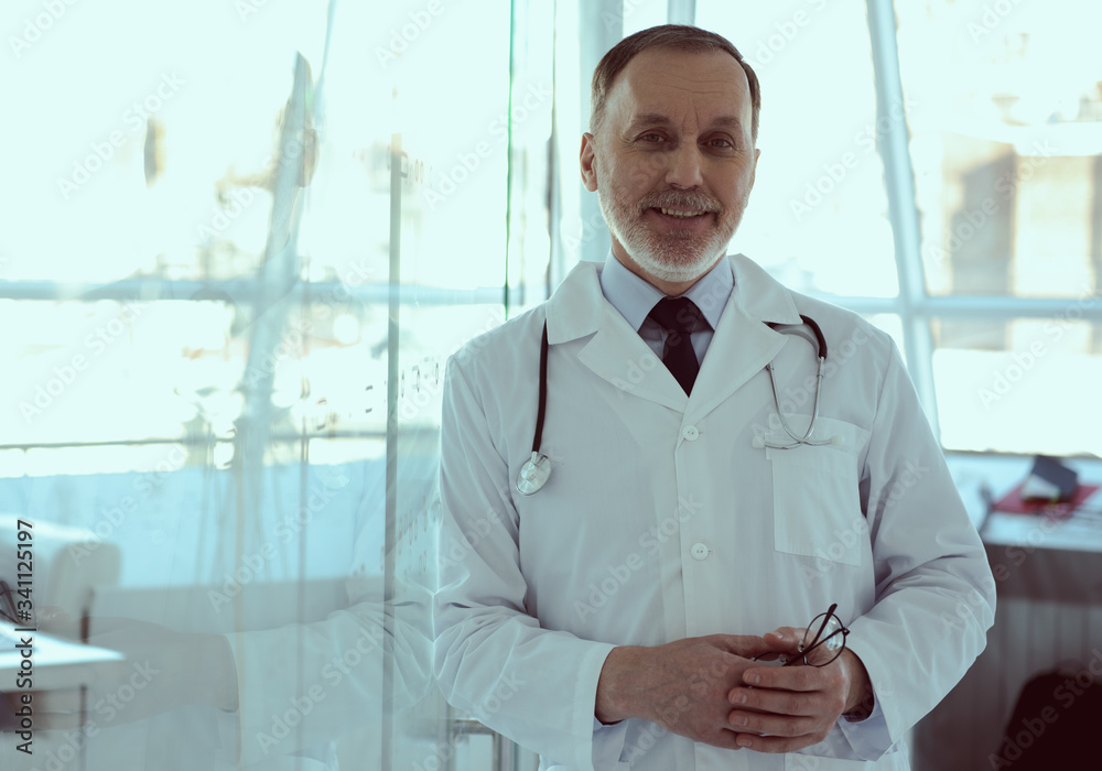 Joyful doctor with stethoscope leaning on glass door