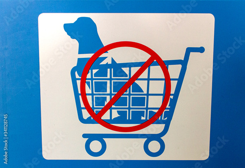 Sign in blue and white with graphic of a dog in a shopping cart indicating No Dogs Allowed In Shopping Carts with red circle backslash no symbol