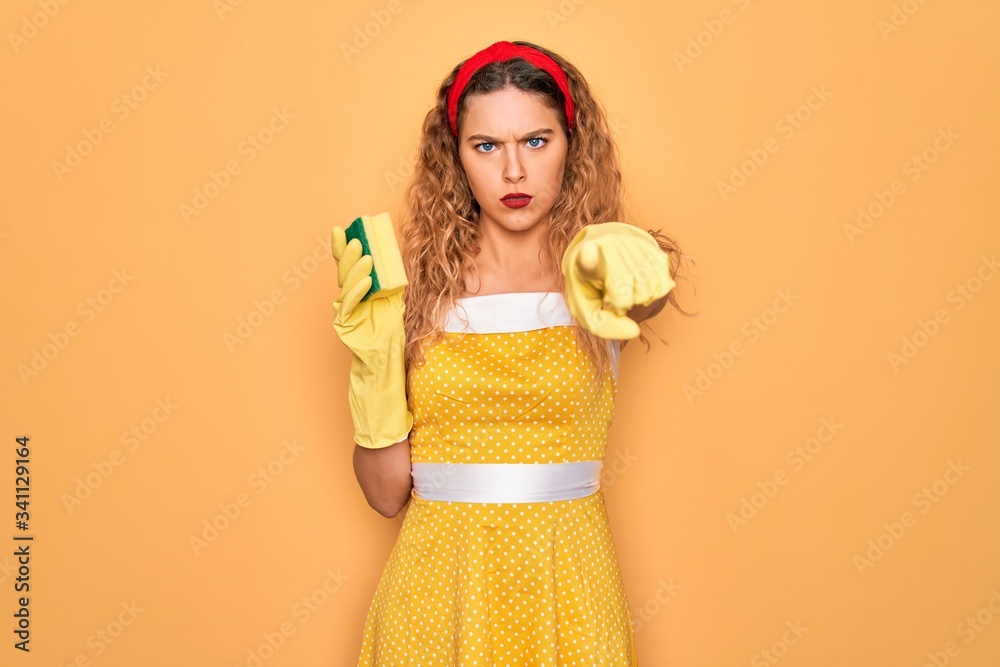 Young beautiful blonde woman with blue eyes cleaning using gloves and cleaner scourer pointing with finger to the camera and to you, hand sign, positive and confident gesture from the front Young beautiful blonde woman with blue eyes cleaning using gloves and cleaner scourer pointing with finger to the camera and to you, hand sign, positive and confident gesture from the front
