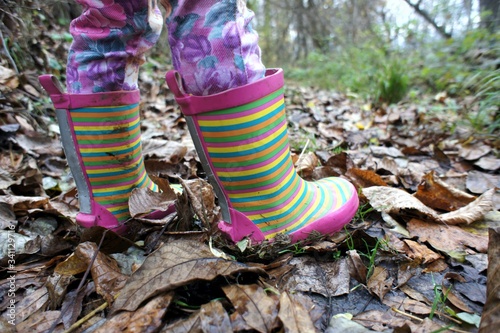 Young Girl in colorful fashion rubber shoes, boots on wet ground covered with autumn leaves  photo