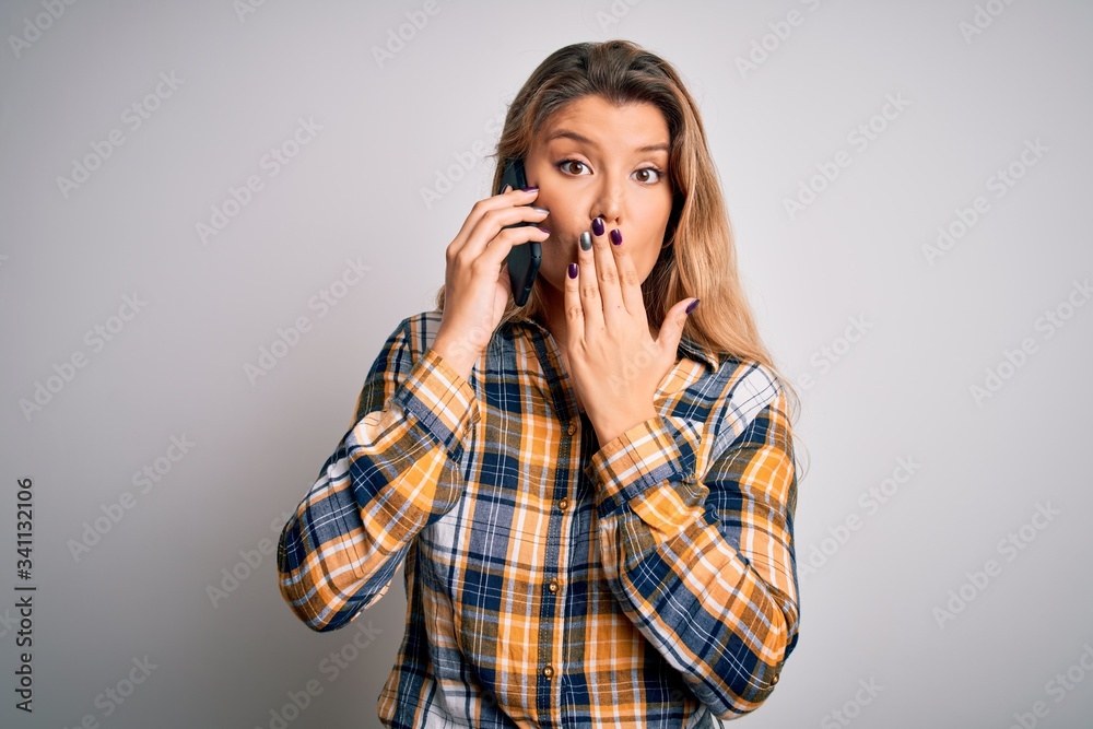 Beautiful blonde woman having conversation talking on the smartphone over white background cover mouth with hand shocked with shame for mistake, expression of fear, scared in silence, secret concept Beautiful blonde woman having conversation talking on the smartphone over white background cover mouth with hand shocked with shame for mistake, expression of fear, scared in silence, secret concept