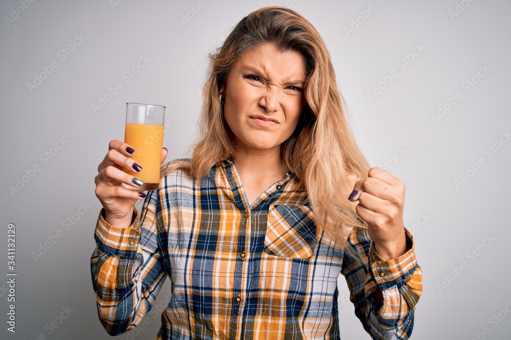 Young beautiful blonde woman drinking glass of healthy orange juice over white background annoyed and frustrated shouting with anger, crazy and yelling with raised hand, anger concept Young beautiful blonde woman drinking glass of healthy orange juice over white background annoyed and frustrated shouting with anger, crazy and yelling with raised hand, anger concept
