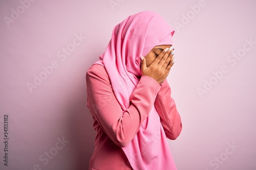 Young African American afro woman wearing muslim hijab over isolated pink background with sad expression covering face with hands while crying. Depression concept. © Krakenimages.com