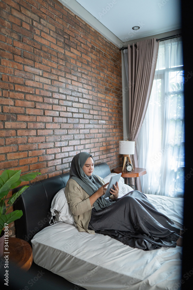 Muslim asian woman using tablet sitting on the bed after prepare and packing clothes