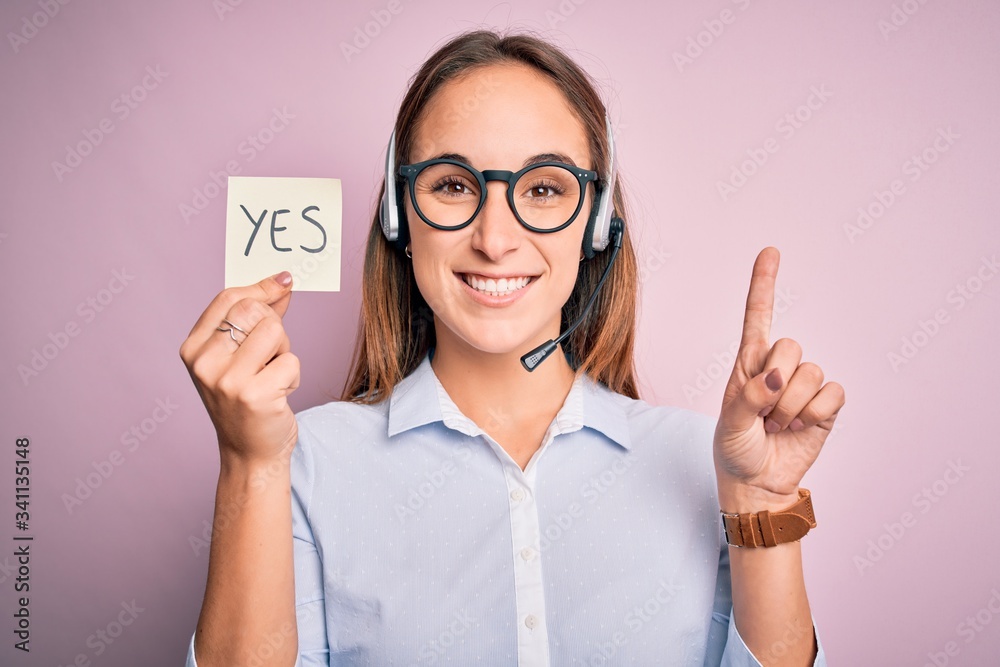 Beautiful call center agent woman working using headset holding reminder with yes message surprised with an idea or question pointing finger with happy face, number one Beautiful call center agent woman working using headset holding reminder with yes message surprised with an idea or question pointing finger with happy face, number one