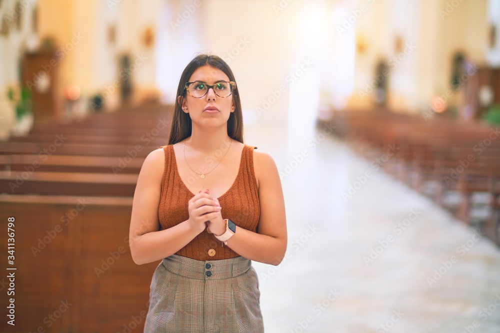 Young beautiful woman standing with hands together praying at church