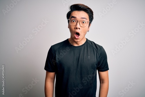 Young handsome chinese man wearing black t-shirt and glasses over white background afraid and shocked with surprise expression, fear and excited face.
