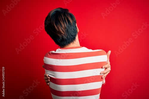 Young handsome chinese man wearing casual striped t-shirt standing over red background Hugging oneself happy and positive from backwards. Self love and self care © Krakenimages.com