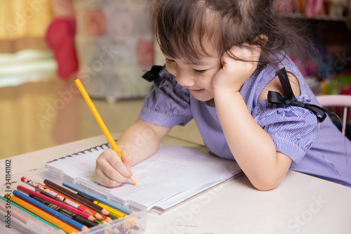 A cute four-year-old Asian girl is sitting and drawing and coloring on her favorite book at home. It develops the skills of preschool children to be ready to study in school and live as they grow up.