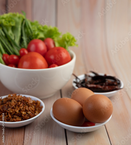 Fried onions, peppers, eggs, tomatoes, salad and spring onions in a white cup on a wooden floor.