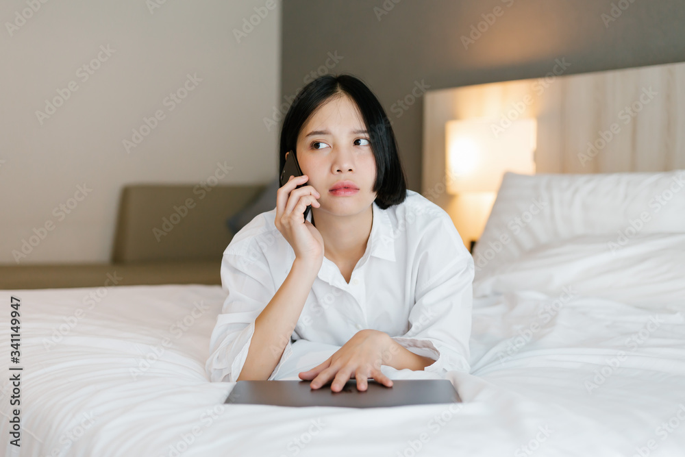 Beautiful asian female in white shirt using mobile phone while working on bed. work from home concept. Beautiful asian female in white shirt using mobile phone while working on bed. work from home concept.