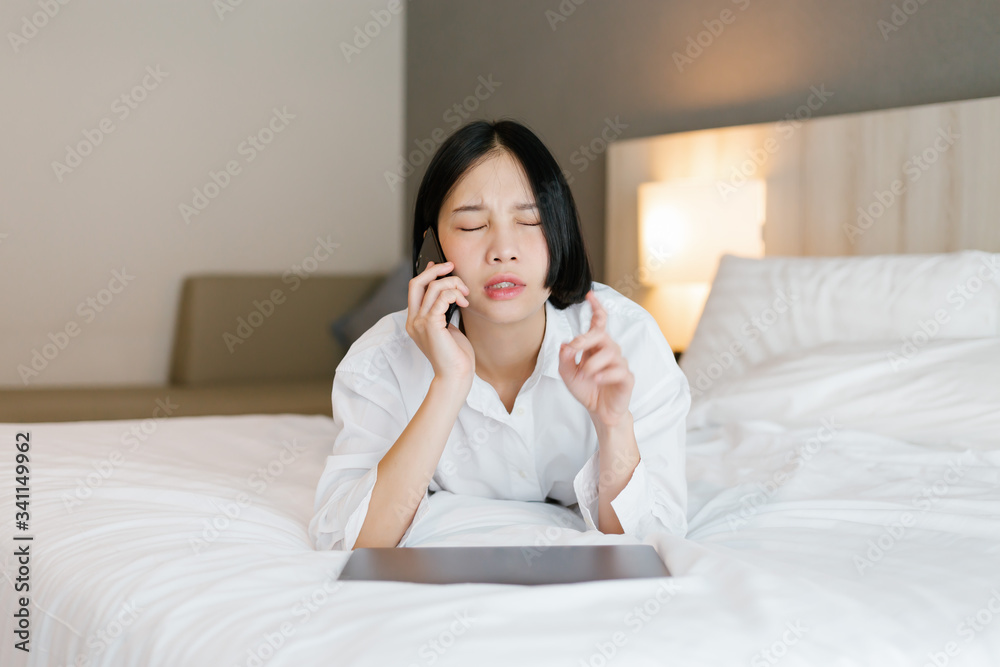 Beautiful asian female in white shirt using mobile phone while working on bed. work from home concept. Beautiful asian female in white shirt using mobile phone while working on bed. work from home concept.