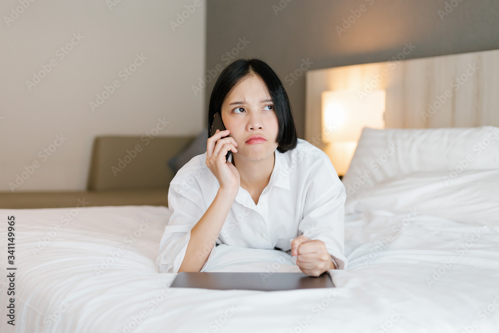 Beautiful asian female in white shirt using mobile phone while working on bed. work from home concept. Beautiful asian female in white shirt using mobile phone while working on bed. work from home concept.