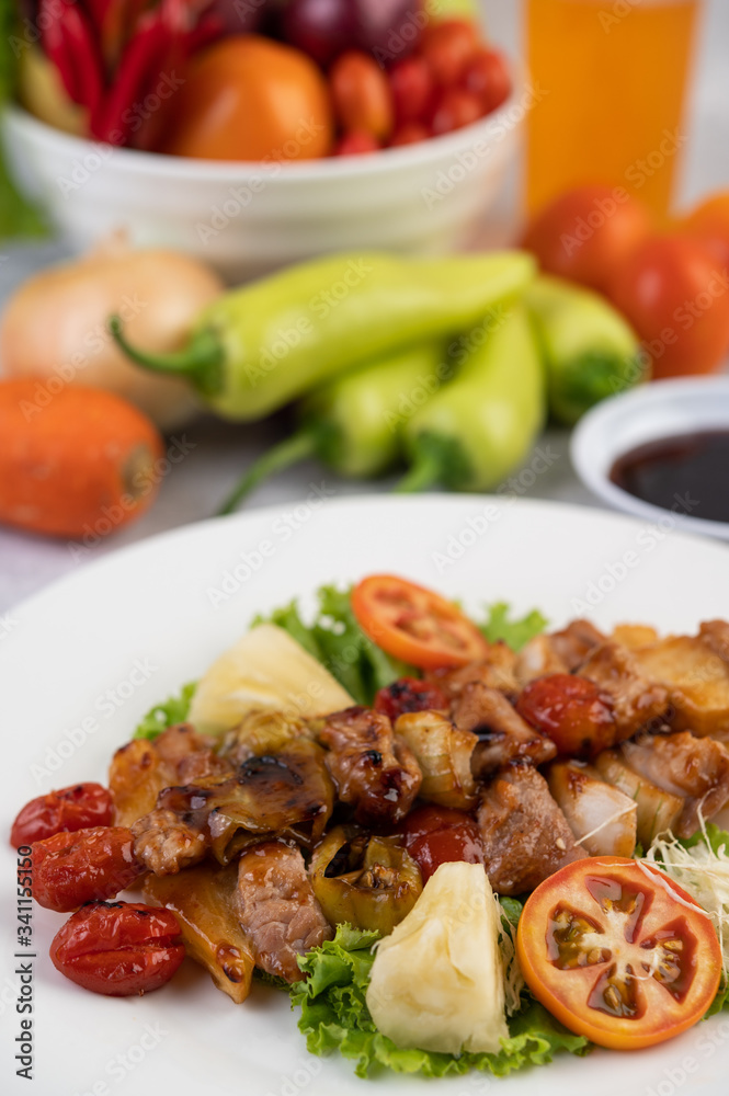 BBQ with a variety of meats, complete with tomatoes and bell peppers on a white plate.