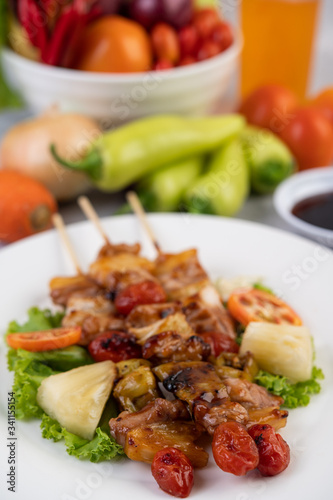 BBQ with a variety of meats, complete with tomatoes and bell peppers on a white plate.