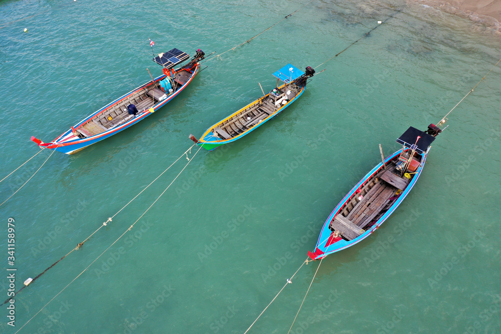 Traditional Asian longtail fishing boats moored beside a sandy beach with palm trees 