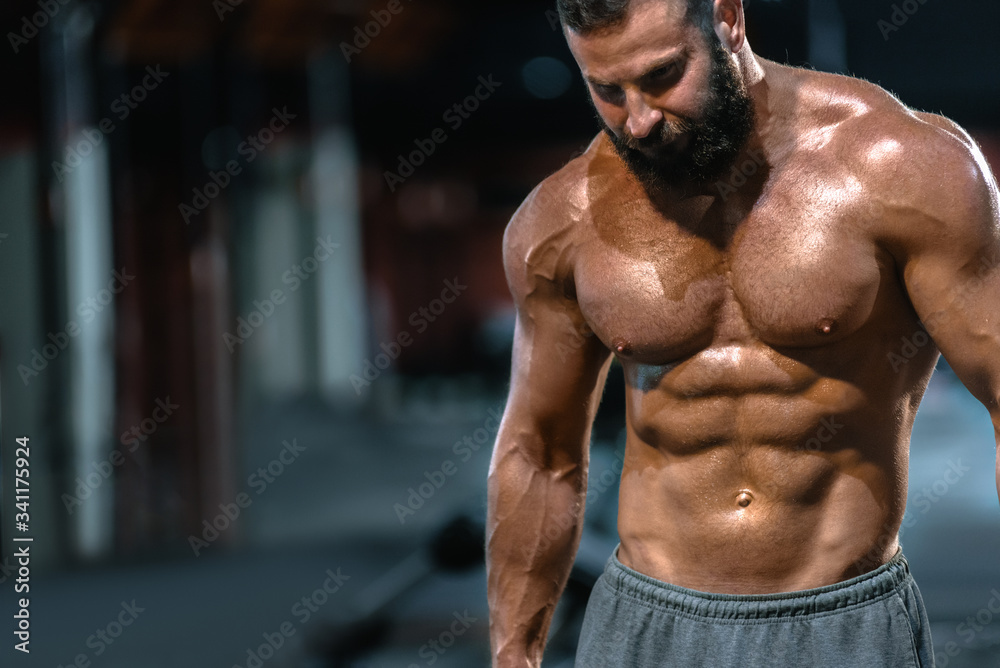 Fototapeta premium Portrait of strong handsome fit man exercising in gym with dumbbells