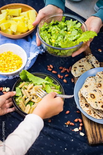 Family eats vegan healthy lunch food together. Woman and daughter kid hands. Salad with lettuce, pasta macaroni, tortilla flatbread and vegetables.