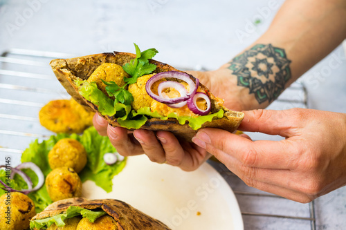 Woman hands hold baked chickpea falafel to eat with hummus, salad leaves and pita bread. Vegan healthy food.  photo