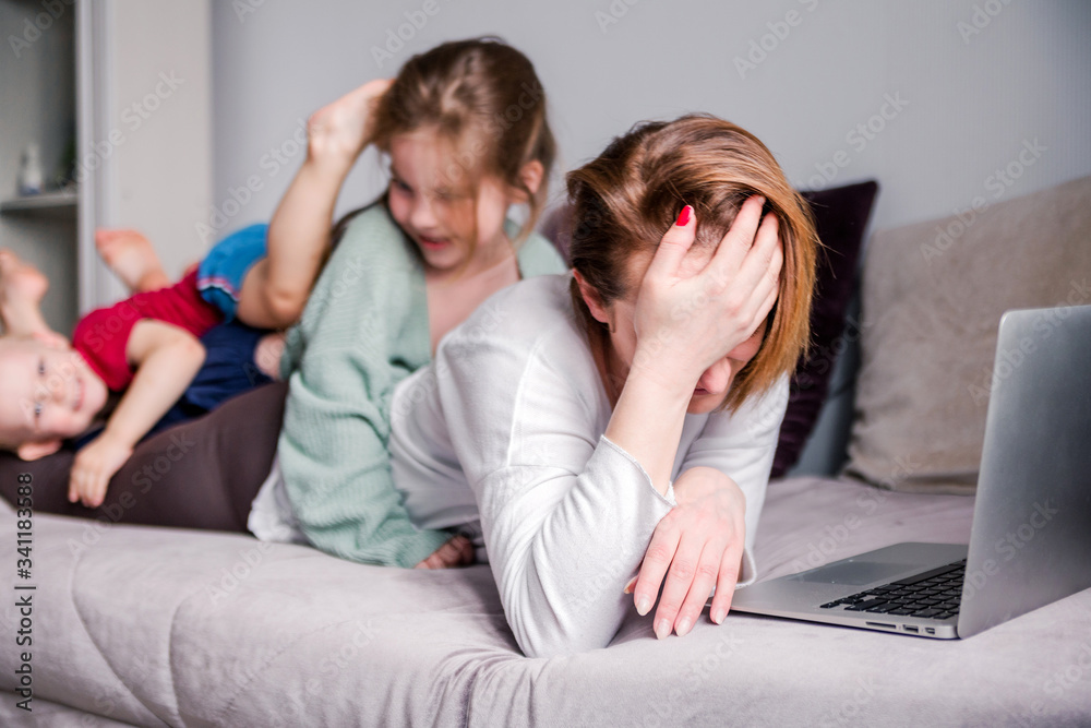 Young women try works at home with laptop along with two children.Children want to communicate with mother, make noise and interfere with work.Self-isolation during coronovirus pandemic Young women try works at home with laptop along with two children.Children want to communicate with mother, make noise and interfere with work.Self-isolation during coronovirus pandemic