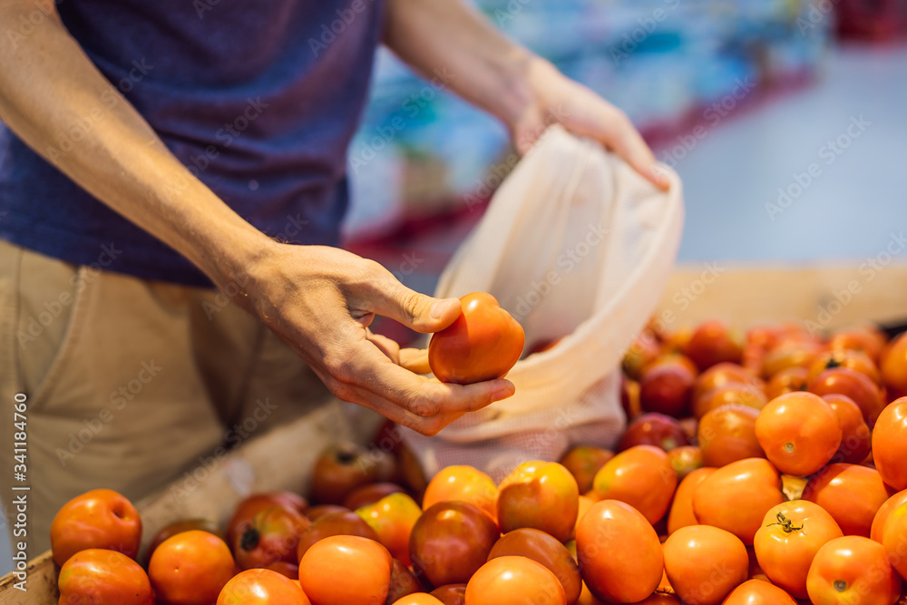 Man chooses tomatoes in a supermarket without using a plastic bag. Reusable bag for buying vegetables. Zero waste concept Man chooses tomatoes in a supermarket without using a plastic bag. Reusable bag for buying vegetables. Zero waste concept