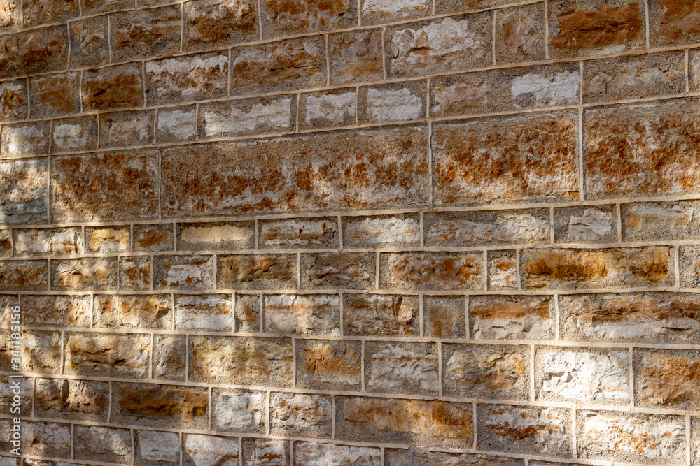 Abstract texture background of a 19th Century brown color natural limestone wall, with tuckpointing mortar restoration, showing filtered tree shadows from low angle sunlight