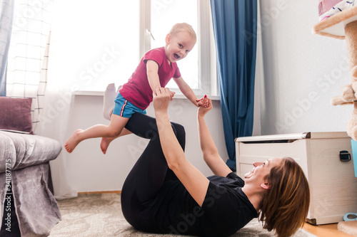 Happy Mother and Child Playing Flying Airplane with Joy while Exercising Pilates, Yoga, Fitness at Home in front of the Laptop