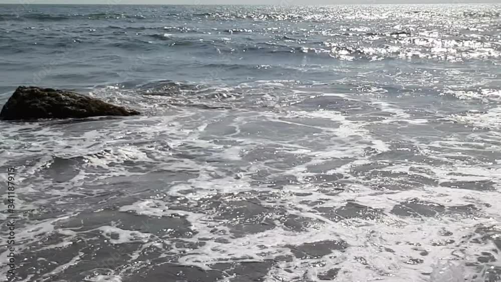 Surf at the sea. Solar highlights on the water surface. The big stone is washed with waves. Surf at the sea. Solar highlights on the water surface. The big stone is washed with waves.