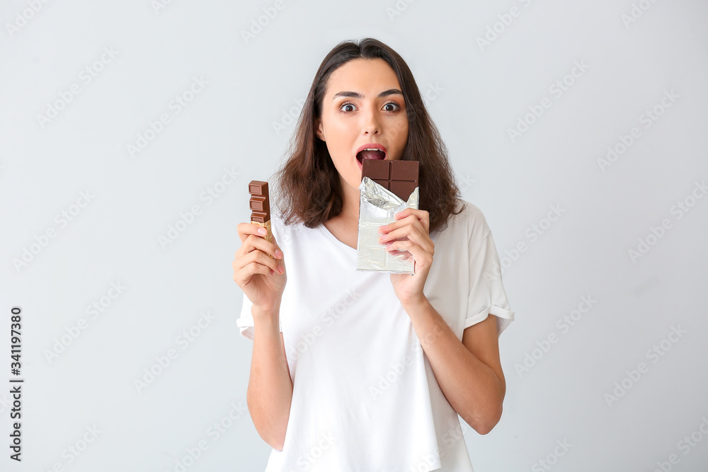 Beautiful young woman eating tasty chocolate on white background Beautiful young woman eating tasty chocolate on white background