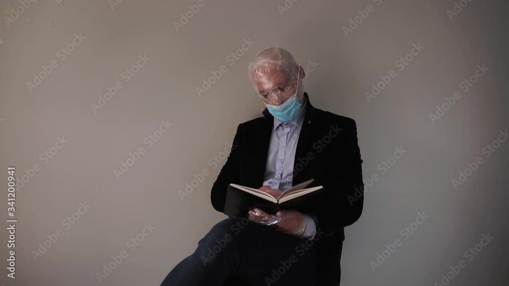 Man dressed in black jacket in protective mask and with face fully rolled up with plastic foil because of over reaction regarding corona virus situation is reading a book Man dressed in black jacket in protective mask and with face fully rolled up with plastic foil because of over reaction regarding corona virus situation is reading a book