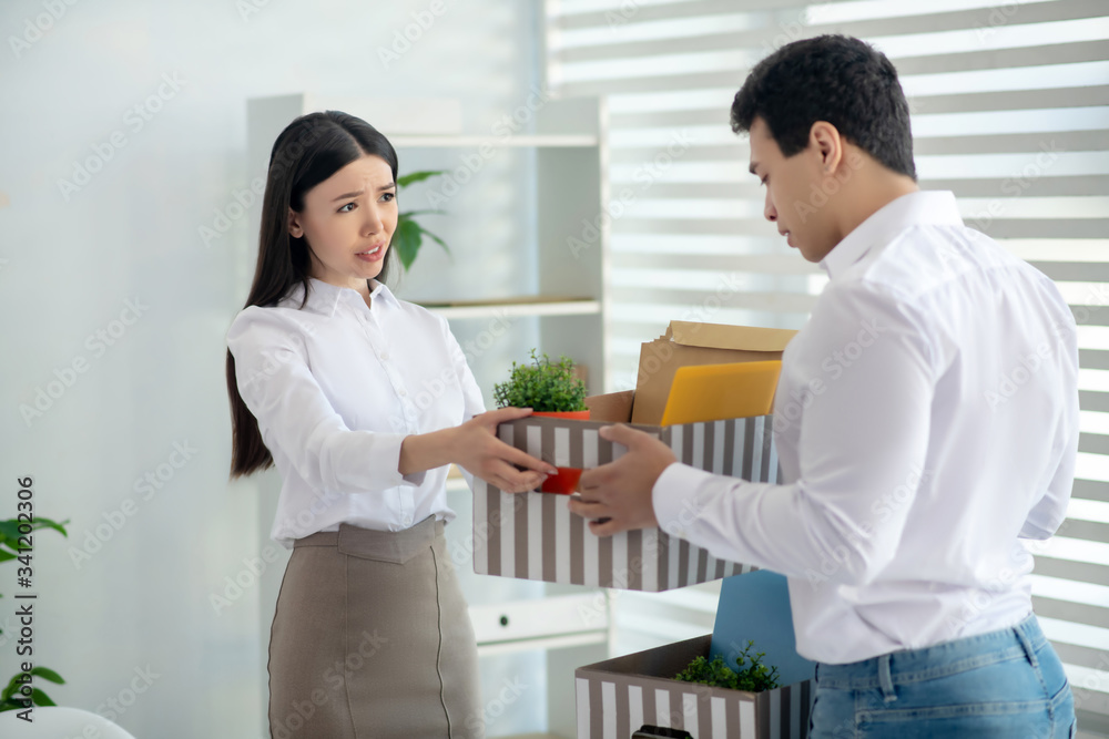 Dark-haired young woman helping her colleague to gather his stuff Dark-haired young woman helping her colleague to gather his stuff