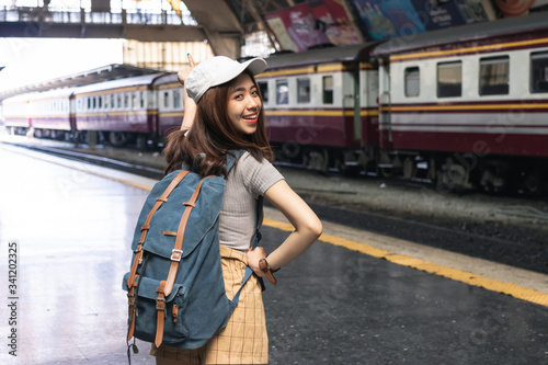 Smiling young Asian backpacker female standing at train station. Summer travel lifestyle concept.