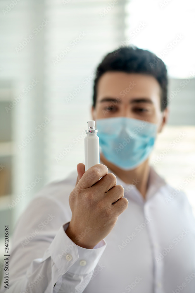 Dark-haired man in a protective mask holding a disinfector in his hand