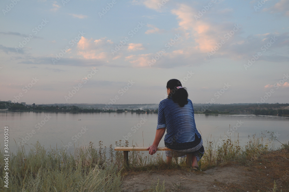 lonely woman sitting on a bench and relaxing by evening lake and sudown clouds