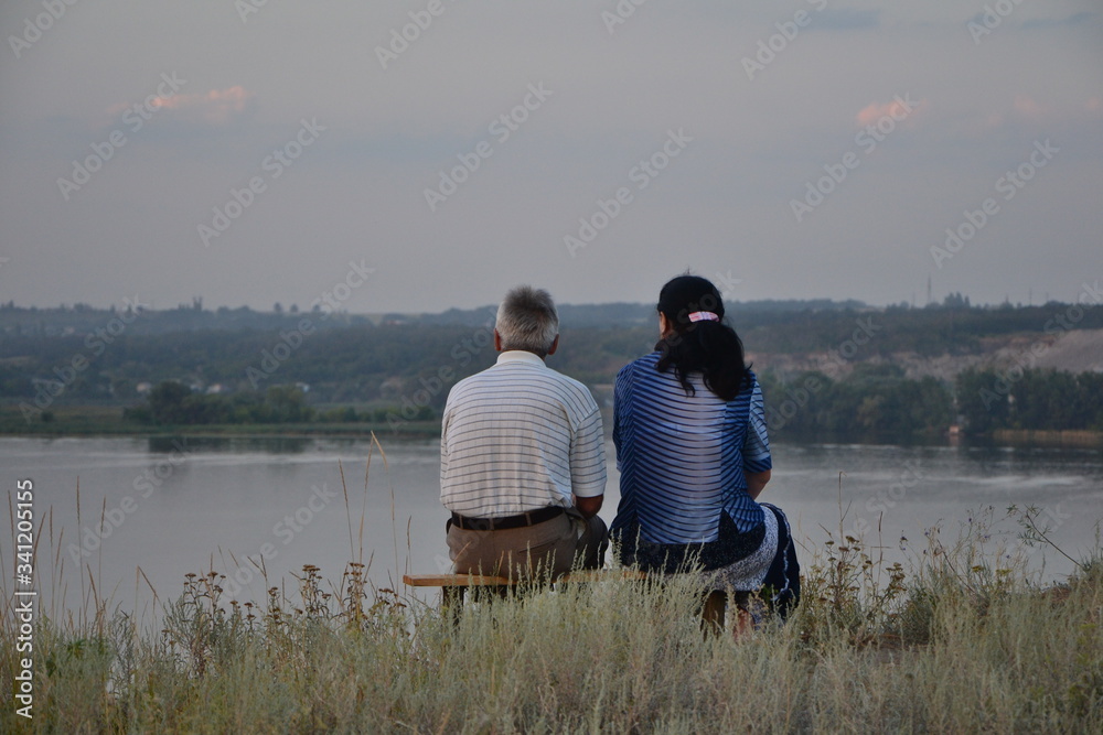 Senior couple sitting on a bench and relaxing by evening lake