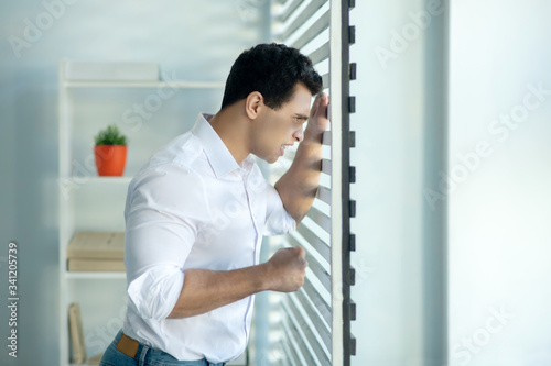 Man looking through the window and looking stressed