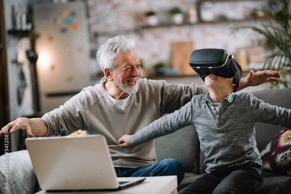 Grandson and his grandpa playing with VR at home on sofa. Grandfather and a little boy having fun at home.
Grandson and his grandpa playing with VR at home on sofa. Grandfather and a little boy having fun at home.