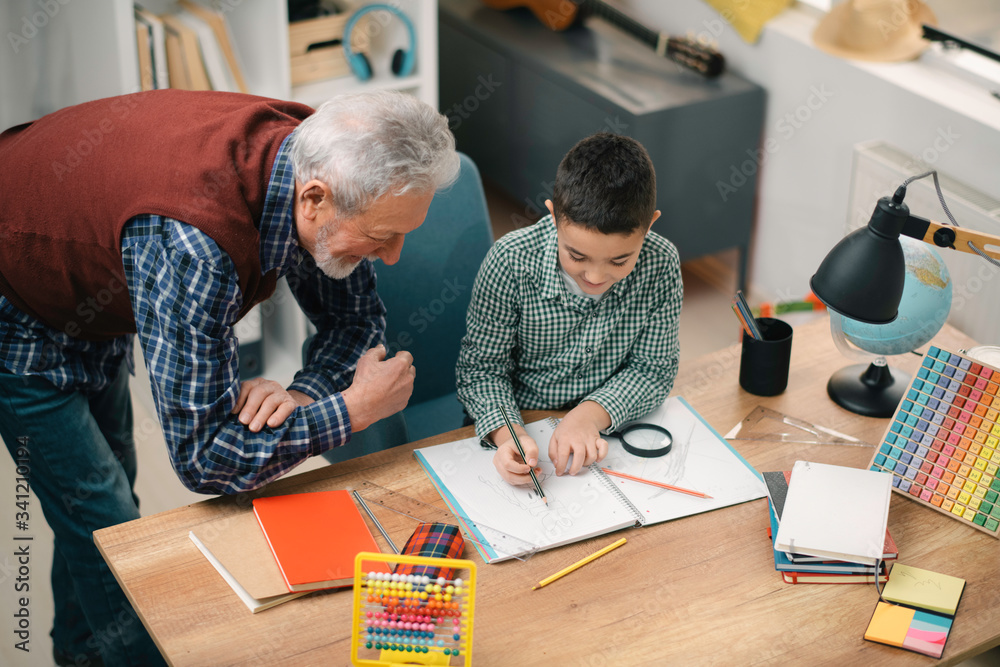 Grandfather and grandson working homework together. Grandpa and grandson enjoying at home. Grandfather and grandson working homework together. Grandpa and grandson enjoying at home.