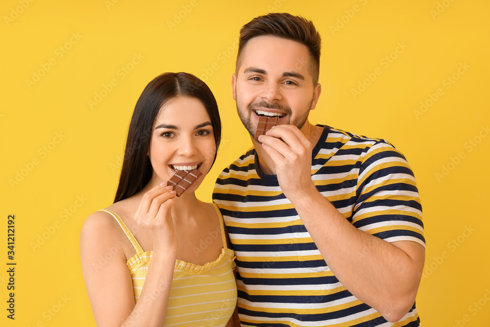 Beautiful young couple with tasty chocolate on color background